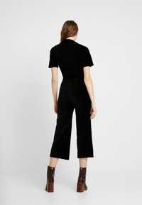 Conjunto de dos piezas de pana negra que incluye una blusa ajustada de manga corta y pantalones de pierna ancha. Combinado con botas de tobillo de tacón marrones.