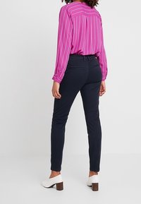 Granatowe obcisłe spodnie o gładkiej fakturze, zestawione z jasnoróżową koszulą w paski z długim rękawem oraz białymi butami na obcasie.