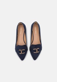 Pump in suede blu navy con punta affusolata e dettaglio in metallo color oro, texture liscia e design elegante. Fodera interna morbida visibile.