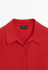 Červená vlněná polo košile s límečkem a pěti knoflíky. Měkká textilie, čistý design s minimálním švem. Obsahuje značkovou štítku uvnitř.