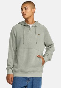 Lichtgroene hoodie met een gestructureerd ribbelontwerp, knoopsluiting bij de kraag en een voorzak. Voorzien van trekkoordjes en aansluitende manchetten.