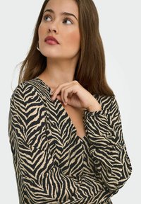 Musterniga mustmustardise ja beezhi värvi topp, mis on kaunistatud zebra-ribadega, V-kujuline kaelus ja pikkade varrukatega, millel on nupukaunistused. Pehme kangast tekstuur.