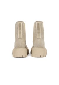 Paire de bottines beige en daim avec semelles en caoutchouc épaisses et rainurées ainsi que des languettes à l'arrière sur fond blanc.