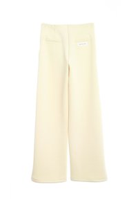 Pantalones de pierna ancha en tejido crema claro, con una textura suave, bolsillos traseros y una pequeña etiqueta en la parte posterior de la cintura.