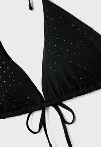 Haut de bikini triangle noir orné de petits sequins noirs et argentés, avec une fermeture à nouer à l'avant, sur fond blanc.