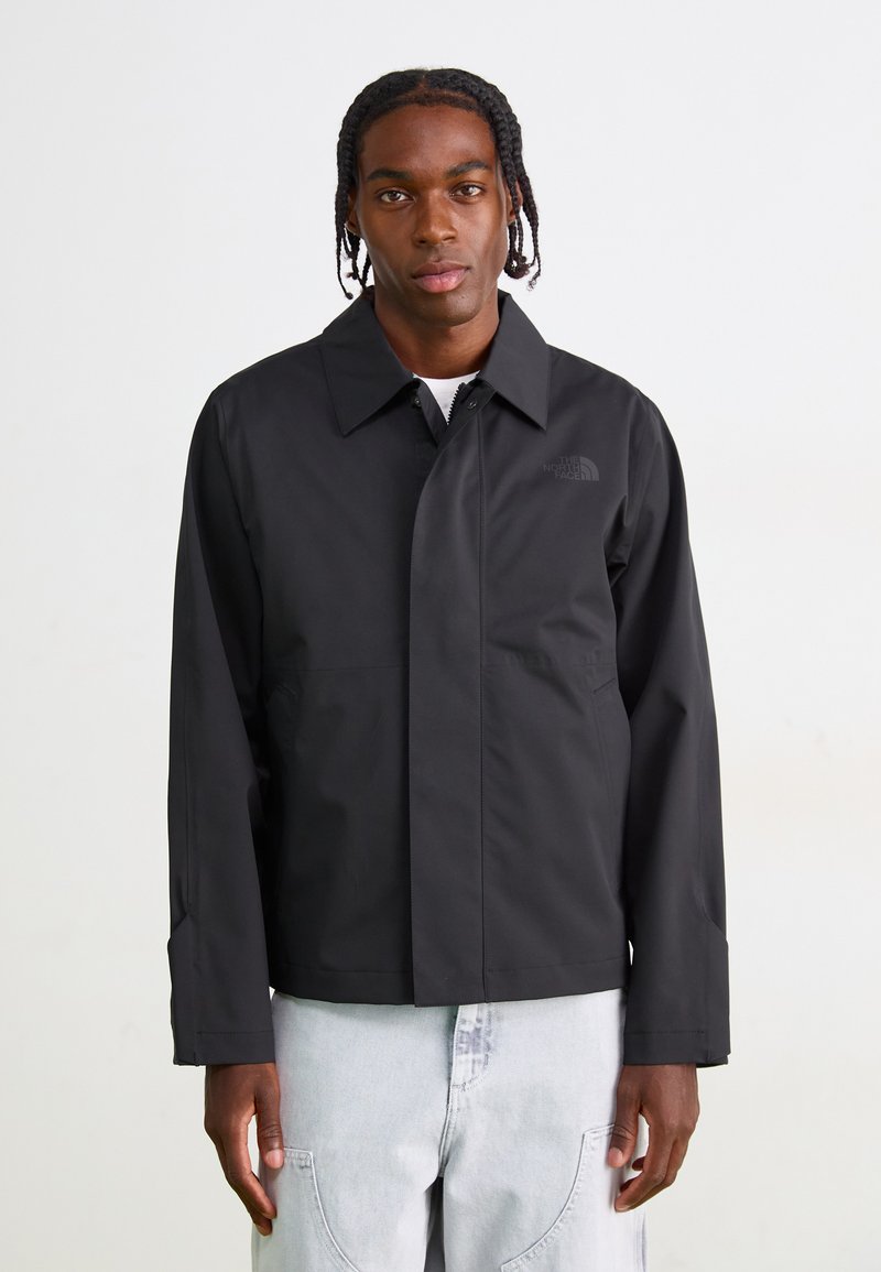 Veste imperméable noire avec un col classique, fermeture éclair à l'avant et un détail logo subtil. Elle possède des manches longues et un design à ourlet droit.