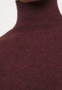 Pull en maille douce et texturée de couleur bourgogne avec col montant ; design ajusté avec des détails côtelés au niveau du col et des épaules.