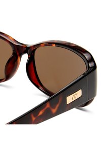 Γυαλιά ηλίου με μοτίβο χελώνας, καφέ φακούς και χρυσή ορθογώνια πλάκα με λογότυπο στο φαρδύ μπράτσο.