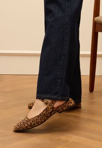 Leopardenmuster-Ballerinas mit spitzer Zehe und seitlichem Riemen mit goldfarbener Schnalle. Glattes Material und flache Sohle. Kombiniert mit dunklem Denim.