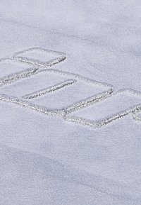 Svijetloplava tkanina s mekom teksturom sadrži srebrne izvezene natpise, prikazujući glatku površinu i suptilni sjaj.