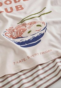 Világos rózsaszín T-shirt, pasztell színekben készült tál tésztás grafikával. A "Tészta Klub" felirat látható rajta, és krém és barna csíkos szegély díszíti.