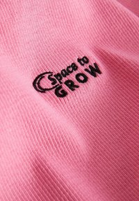 Roza bombažna oblačila z teksturirano rebrasto površino, ki ima črno vezeno besedilo "prostor za RAST."