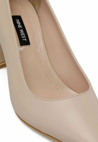 Beige kõrge kontsaga king, millel on sile sünteetiline ülemine osa, terav varvas ja pehmendusega sisetald. Omab tagasihoidlikku platvormi ja tekstuurset tallat.