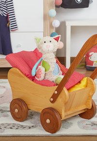 Wooden toy stroller with red and yellow cushions holding a colorful patchwork stuffed cat in a child's room.