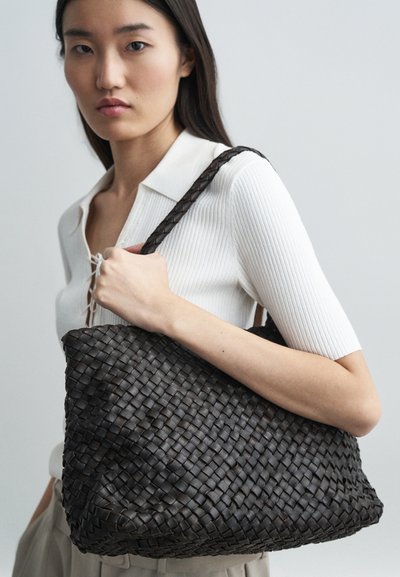 Πλεγμένη τσάντα ώμου από σκούρα καφέ δέρμα με υφή, διαθέτοντας πλεκτό λουρί και ευλύγιστο, χαλαρό σχήμα.