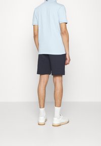 Polo shirt azzurro chiaro, pantaloni corti blu navy, sneaker bianche con suola in gomma. Texture liscia, vestibilità classica, dettagli include colletto e maniche corte.