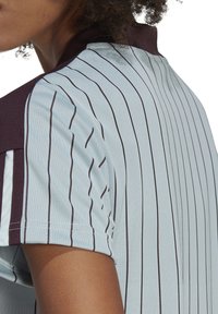 Polo shirt rayé bleu clair avec un col foncé. Il présente des manches courtes et une texture respirante. Des lignes verticales décorent le tissu.