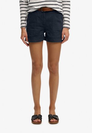 Kvinde iført marineblå shorts med opsmøg, brun bælte, sorte slip-on sandaler og en langærmet hvid top med sorte vandrette striber.