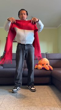 Κόκκινο φουντωτό μαντήλι που κρατάει ένα άτομο με γκρι φούτερ με φερμουάρ και μαύρο τζιν, με μια μαλακή χταποδίτσα να κάθεται σε έναν καναπέ.