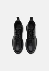 Botas de tobillo de cuero negro con textura suave, puntera redonda y diseño de cordones. Presentan una lengüeta en la parte trasera y una suela de goma.