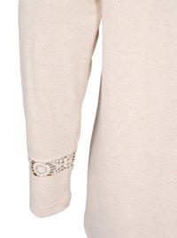 Camicia beige a maniche lunghe con un accento in pizzo all'uncinetto sui polsi. Tessuto morbido con una finitura liscia, senza motivi o accessori visibili.
