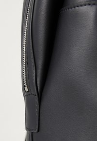 Black leather backpack with a smooth texture, featuring a silver zipper and subtle embossed accents on the side.