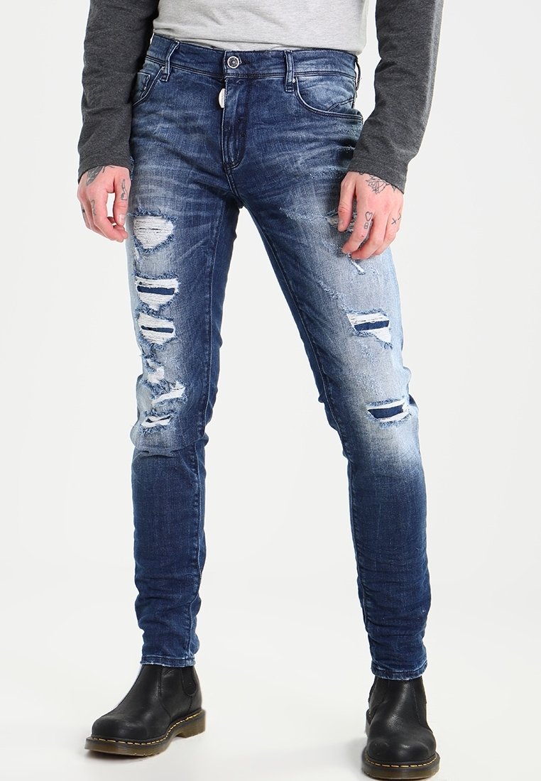 Faded blue jeans with distressed rips, slim fit, five-pocket design, and metal button closure. Worn with black ankle boots.