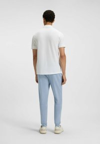 Biała koszulka polo z krótkim rękawem, zestawiona z jasnoniebieskimi, zwężanymi spodniami. Stylizację dopełniają beżowe sneakersy.