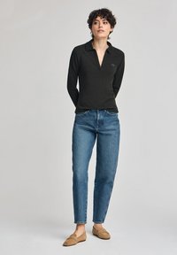 Dark green long-sleeve polo shirt with a slight collar, paired with light blue straight-leg jeans and beige loafers. Simple, casual look.