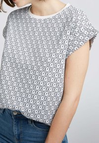 Haut à manches courtes avec un motif géométrique noir et blanc, fabriqué en tissu léger. Encolure ronde et coupe décontractée.