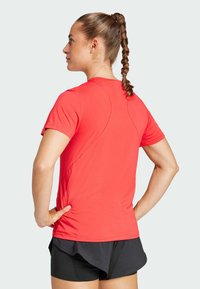Red athletic t-shirt with short sleeves and a rounded neckline, featuring textured stitching details along the back and shoulders.