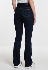 Jeans acampanados de mezclilla en azul oscuro con costuras amarillas. Presentan una cintura alta, cinco bolsillos y una pequeña etiqueta de la marca en el bolsillo trasero.