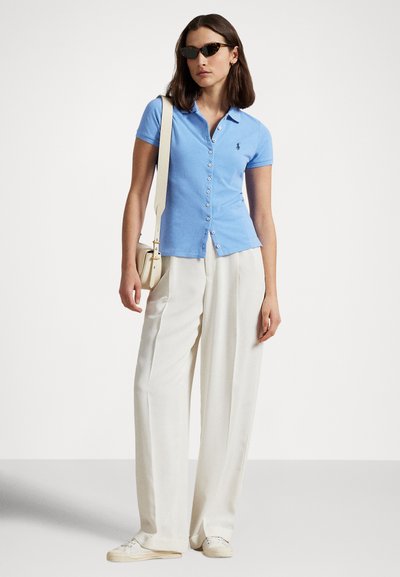 Svetlo modra polo majica z gumbi na sprednji strani, kratkimi rokavi in logotipom. Kombinirana s kremasto širokimi hlačami in belimi športnimi copati.