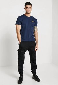 Marineblå t-skjorte med korte ermer og en liten gul logo, kombinert med svarte cargosbukser med lommer, elastiske cuffs og en avslappet passform.