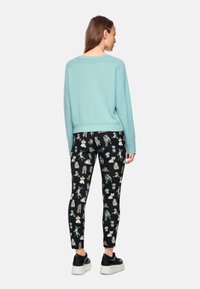Hellblaues Sweatshirt mit lockerer Passform und gerippten Bündchen, kombiniert mit schwarzen Leggings mit buntem, verspieltem Tierdruck. Schwarze Sneakers.