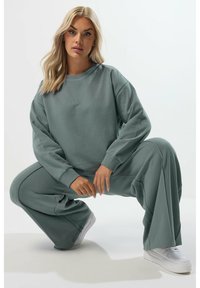 Ljusgrön, oversized sweatshirt och matchande vida byxor. Mjuk tyg, ribbade mudd och en avslappnad passform. Vita sneakers.