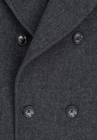 Dwurzędowy płaszcz w ciemnoszarym wzorze w jodełkę z wełny. Posiada duże czarne guziki oraz fakturowany materiał, z szerokim wzorem kołnierza.