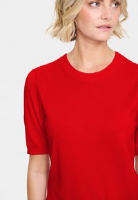 Maglione corto a maniche corte di colore rosso, con colletto rotondo a costine, superficie liscia e silhouette aderente.