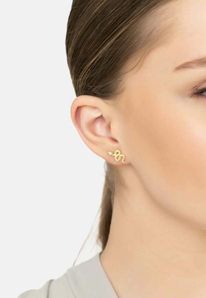 Gold snake-shaped earring with a textured surface, displayed on an ear. The design features curves and a shiny finish.