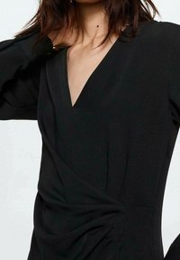 Schwarze Wickelbluse mit tiefem V-Ausschnitt, langen Ärmeln und raffung an der Taille, aus glattem Stoff gefertigt.