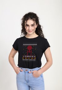 Camiseta corta negra con estampado gráfico rojo que presenta estrellas y el texto "A ATREVERSE A IR" en blanco y amarillo, combinada con pantalones vaqueros de un azul claro.