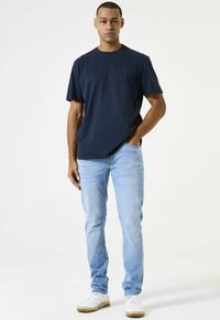 Camiseta azul marino de cuello redondo y mangas cortas, combinada con jeans de color azul claro y zapatillas blancas. Diseño sencillo, ajuste casual.