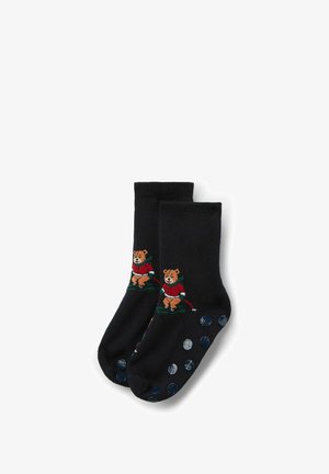 Schwarze Socken mit einem gestickten Bären in roten Outfit und grünen Akzenten. Die Sohlen sind mit blauen Punkten für Grip und Textur versehen.