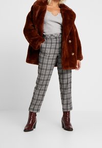 Ruske fau fur jakke med stor krave og gyldne knapper, kombinert med svart og hvit rutete høy midje bukser og burgunder ankel støvler.