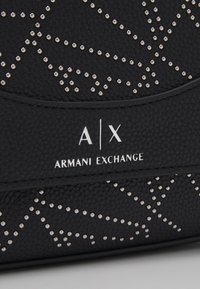 Zwarte leren tas met een gestructureerd oppervlak, gespreide zilveren accenten in een geometrisch patroon en een prominent wit logo met "ARMANI EXCHANGE."