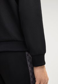 Zwarte sweatshirt met ribgebreide manchetten, gecombineerd met zwarte broek met een gestructureerd patroon en een contrasterend grijs ontwerp aan de zijkant.