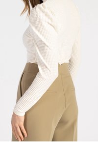 Vit texturerad långärmad topp med passform som framhäver midjan och utsvängda axlar, ihop med beige skräddarsydda byxor med bakfickor.