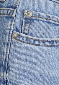 Tessuto in denim blu chiaro con una trama testurizzata, dotato di hardware argentati su una tasca frontale e dettagli di cucitura a contrasto.