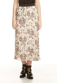 Donna che indossa una gonna midi plissettata crema con un motivo floreale rosa e blu e stivaletti neri alla caviglia con grandi fibbie dorate.