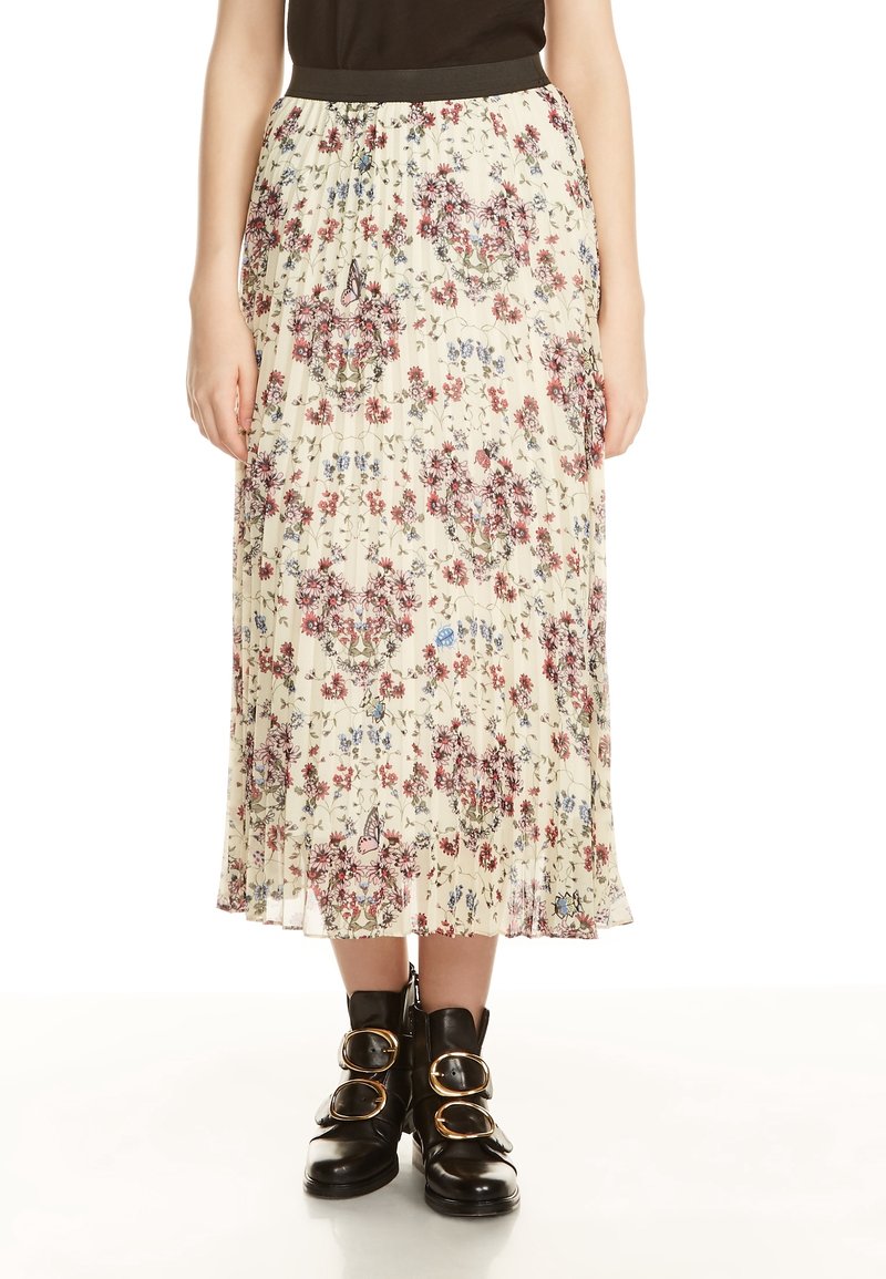 Donna che indossa una gonna midi plissettata crema con un motivo floreale rosa e blu e stivaletti neri alla caviglia con grandi fibbie dorate.